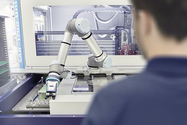 Teamwork in der Elektronikindustrie: Bei diesem Nutzentrenner unterstützt ein Roboterarm mit einem Greifer den Bediener bei der Beladung.