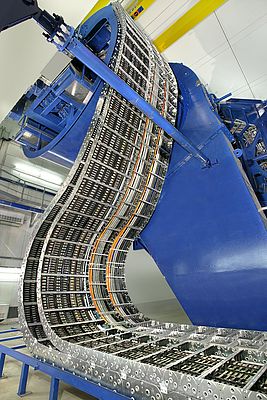 Für eine Gantry in einem Ionenstrahl-Therapiezentrum sind verschieden große Stahlketten in Mehrbandanordnung, kombiniert mit Kunststoffketten, so angeordnet, dass eine kreisförmige Bewegung möglich ist.
