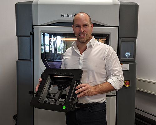 Stefan Kammann vor dem Fortus 450mc 3D-Drucker im ADaM Competence Center mit einer 3D-gedruckten, ESD-konformen Klebevorrichtung.