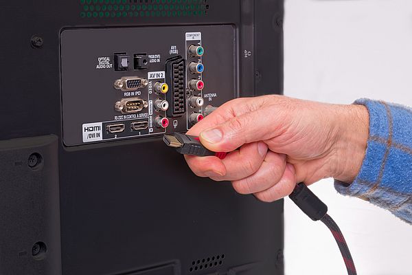 Hand holding HDMI cable in the back of an HDTV box